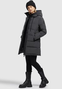 Zwarte gewatteerde parka met een capuchon, voorzien van een ritssluiting en aantrekkoordjes. Draagover een zwarte legging en krachtige zwarte combatlaarzen.
