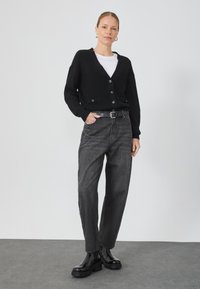 Cardigan nero a maglia con scollo a V e bottoni, abbinato a jeans in denim grigio a vita alta e stivaletti neri. Design semplice, vestibilità comoda.
