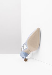 Sandale à talons hauts bleue avec une finition lisse, des fines lanières et une semelle beige texturée. Le talon mesure environ 10 cm de haut.