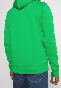 Felpa verde realizzata in tessuto morbido, con cappuccio regolabile, polsini e orlo a coste, dalla vestibilità rilassata e dalla texture liscia.