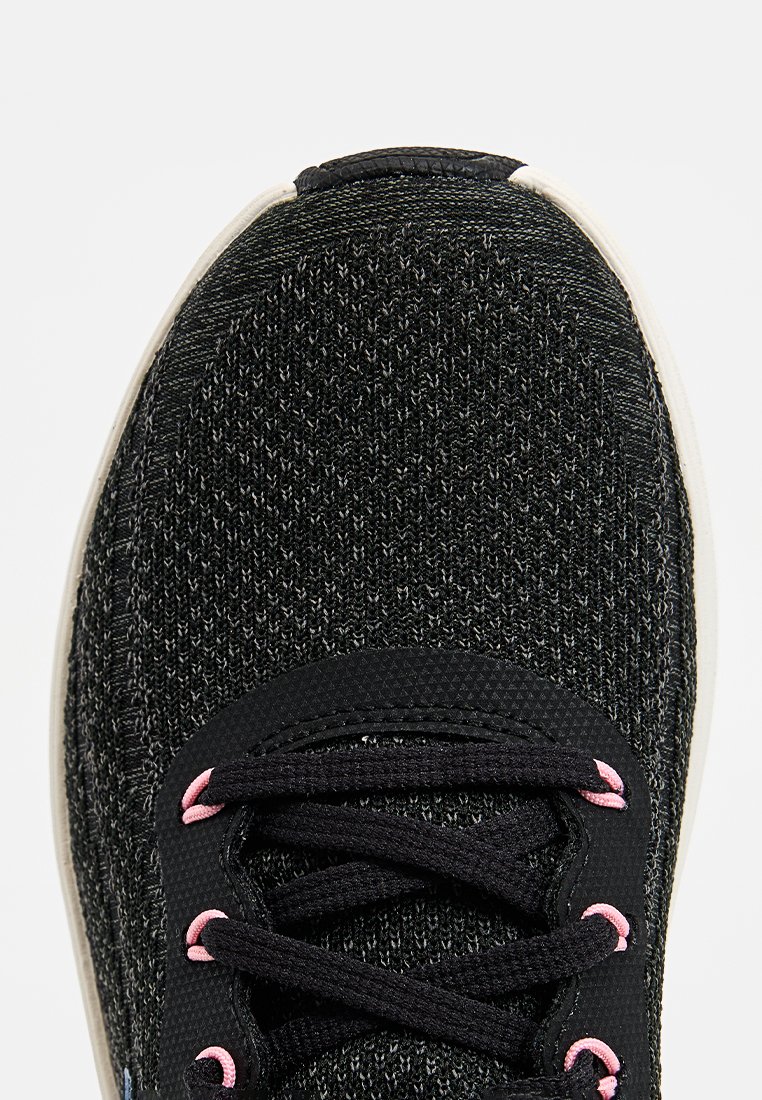 Zapatilla deportiva negra con parte superior de punto texturizado, que cuenta con cordones negros y ojales rosa claro, y una suela de goma blanca.