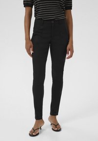 Svarta slim-fit-byxor med en slät textur, framfickor och en enkel knappstängning. Kombinerat med en svart och vit randig topp.