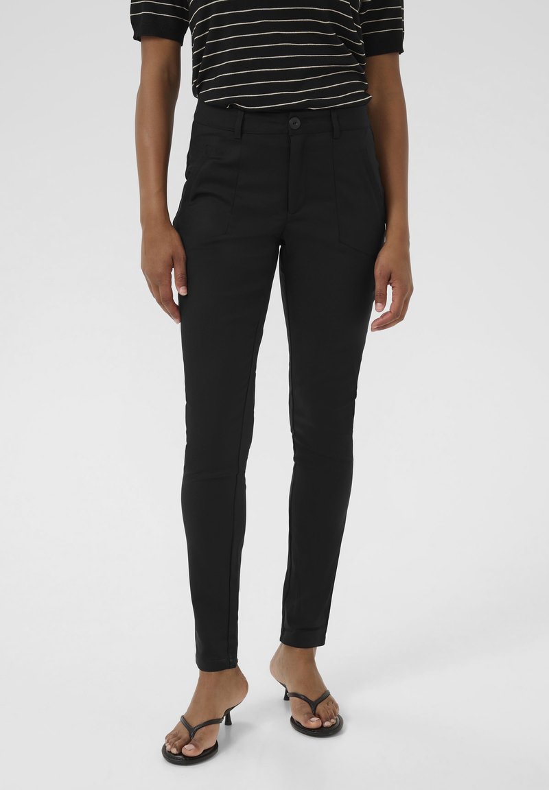 Svarta slim-fit-byxor med en slät textur, framfickor och en enkel knappstängning. Kombinerat med en svart och vit randig topp.