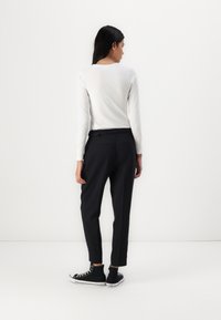 Pantalons noirs ajustés à taille haute, avec des poches latérales et une coupe droite, associés à des baskets montantes noires et une chemise blanche à manches longues.