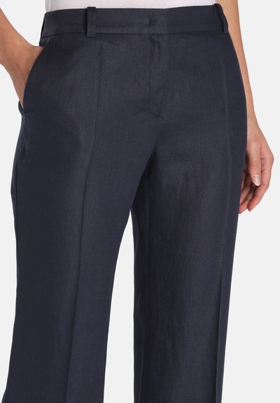 Pantalon ajusté bleu marine avec poches latérales porté avec un haut blanc, doté d'un devant plat et de passants pour ceinture.