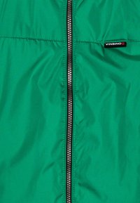 Giacca verde con una texture liscia e lucida, dotata di una cerniera centrale e di una piccola etichetta di marca nera sul lato sinistro.