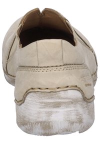 Chaussure beige clair à enfiler avec une tige en cuir texturé, des coutures visibles et une semelle superposée blanche brute. Design à bout rond.