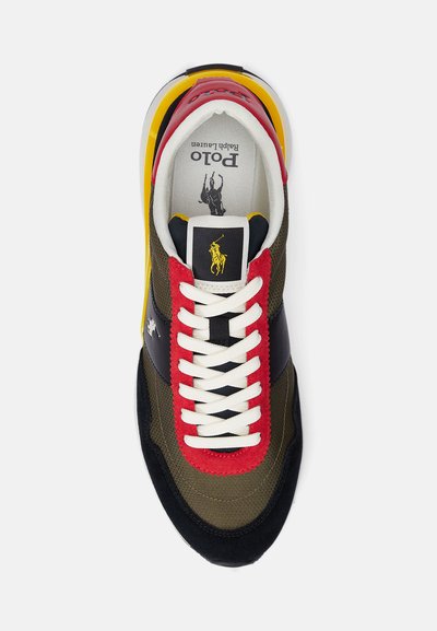 Zapatilla que presenta una mezcla de materiales en verde oliva, negro, rojo y amarillo. Tela texturizada con cordones blancos y detalle del logo en la lengüeta.