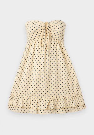 Schulterfreies, beiges Sommerkleid mit marineblauen Punkten, einer Bindeschleife vorne und einem gerafften Saum, auf einem einfarbigen Hintergrund präsentiert.