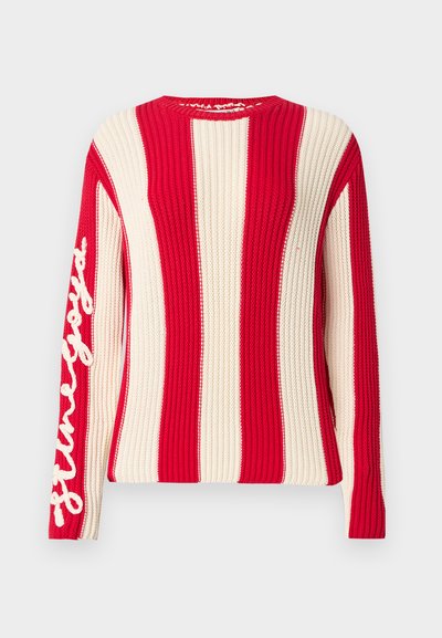 Πλεκτό πουλόβερ με μακριά μανίκια, φαρδιές κάθετες κόκκινες και εκρού ρίγες και λευκό κείμενο με πλάγια γραφή στο αριστερό μανίκι.