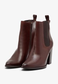 Bottes chelsea en cuir marron avec un bout pointu, fermeture éclair et panneaux latéraux élastiques. Présente un talon épais et une texture lisse.