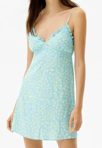 Ljusblå klänning med ett blommönster i gulaktiga nyanser, med tunna spagettiband och volangkanter längs halsringningen.