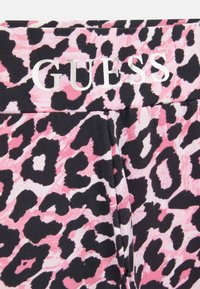 Legíny s tlačou čiernych a ružových leopardov s mäkkou textúrou a elastickým pásom; na vrchu sa nachádza logo "GUESS" v striebornej farbe.