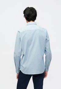 Camisa azul clara de manga comprida feita de tecido macio, com colarinho padrão e punhos com botões, bainha curva e textura minimalista.