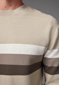 Suéter beige con rayas horizontales en crema claro, topo y marrón oscuro. Tejido texturizado con cuello acanalado. Vista en primer plano.