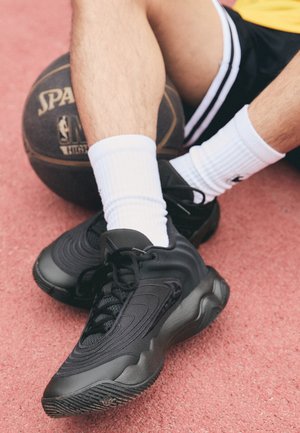 Beine mit schwarzen Turnschuhen und weißen Socken ruhen auf einem Basketball auf einer roten Außenplatzoberfläche.