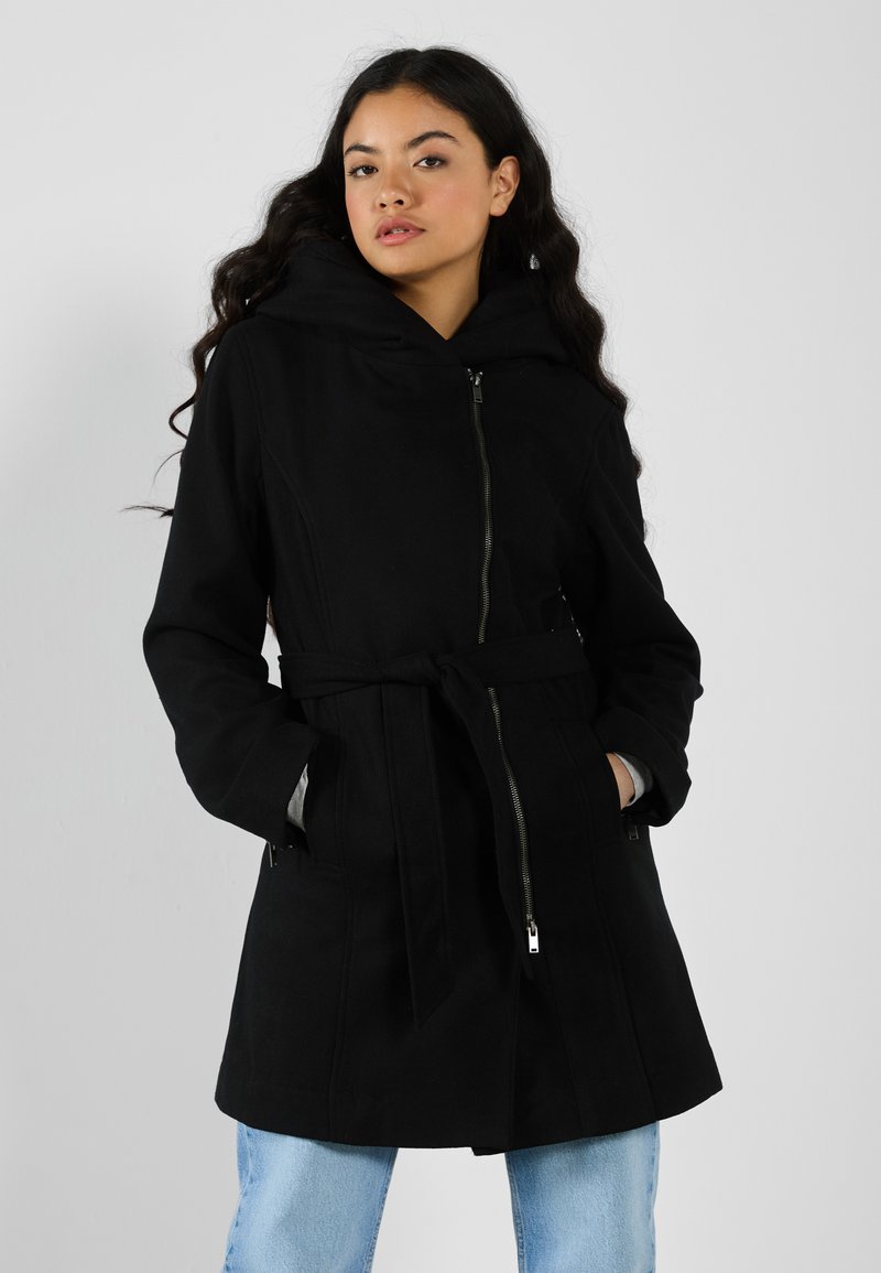 Manteau noir à capuche avec une taille cintrée, fermeture éclair sur le devant et deux poches latérales. Le tissu est lisse et le design présente un ourlet évasé.