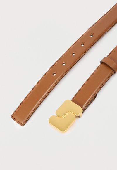 Ζωνάρι από ταμπά δέρμα με ραμμένα άκρα και πολλές τρύπες, διακοσμημένο με μεγάλη, λαμπερή χρυσή πόρπη με αφηρημένο γεωμετρικό σχέδιο.