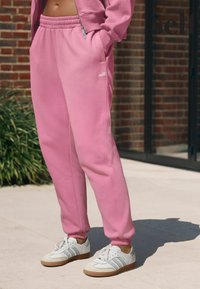 Ružové bavlnené tepláky s elastickým pásom a bočnými vreckami, doplnené o biele tenisky so sivými pruhmi a gumovou podrážkou.