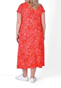 Czerwona maxi sukienka w wzór paisley z krótkimi rękawami; wykonana z miękkiego materiału i o luźnym kroju. Połączona z białymi trampkami.