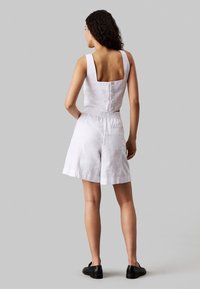Conjunto de dos piezas de lino blanco que incluye un top corto de espalda cuadrada y pantalones cortos con cintura elástica, con un diseño minimalista y sin patrones visibles.