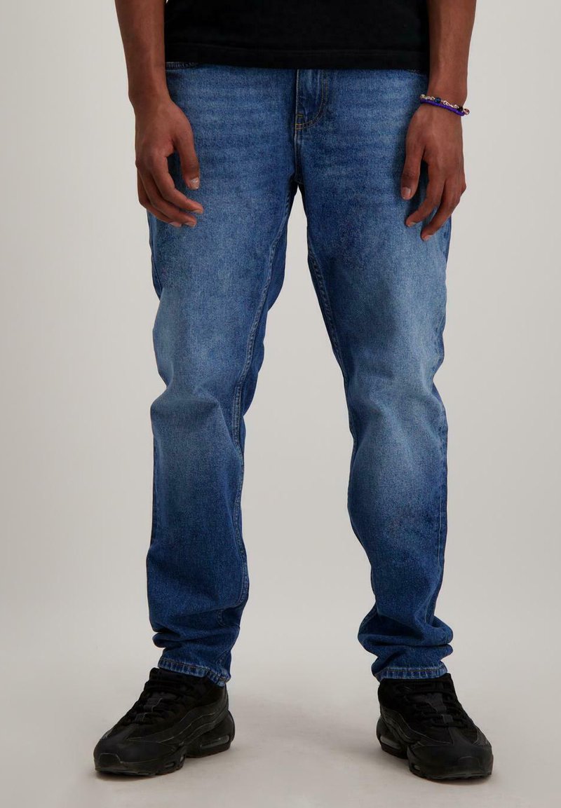 Blauwe spijkerbroek met een relaxte pasvorm, voorzien van een medium wasbeurt, lichte vervaging en rechte pijpen. Gepaard met zwarte sportschoenen.