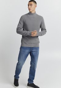 Grå strikket høyhalset genser med ribbet struktur, kombinert med blå denimjeans og sorte sneakers. Enkelt design med lange ermer.