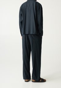 Marineroze, lichte, langemouwen shirt met een relaxte pasvorm, gecombineerd met bijpassende brede-pijpbroeken. Sandalen hebben donkere banden en een kurken zool.