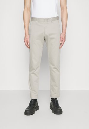 Beige Chinos mit schlankem Schnitt, aus Baumwollmaterial und glatter Textur. Das Kombinieren mit schwarzen Schnürschuhen sorgt für einen Kontrast.