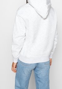 Grijze hoodie met een zachte textuur, voorzien van een buidelzak en geribbelde manchetten. Gecombineerd met lichtblauwe spijkerbroek.