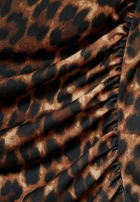 Tela de estampado de leopardo que presenta una mezcla de colores marrón, negro y tostado. El material tiene una textura suave con detalles fruncidos a lo largo de un borde.