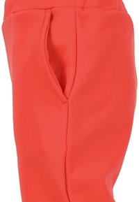 Pehmeästä ja joustavasta kankaasta valmistetut korallinväriset verkkarit. Niissä on sivutasku piilotetulla aukolla ja sileä sauma detailing.