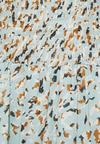Tissu de robe bleu clair avec un motif abstrait éparpillé en orange, noir et blanc. Texture smockée avec des détails plissés.