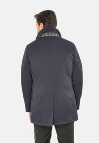 Cappotto imbottito blu scuro con colletto alto e fodera a quadri. Presenta un taglio dritto e dettagli di cucitura sottili sulle maniche e sul retro.