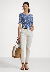 Top fitted a fiori blu con maniche a 3/4, abbinato a jeans skinny bianchi e sandali platform color cammello. Tiene una borsa a tracolla di paglia.