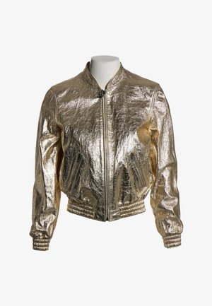 Chaqueta bomber dorada metálica con cremallera frontal, bolsillos laterales con cremallera, puños elásticos y cintura, mostrada en un torso de maniquí blanco.
