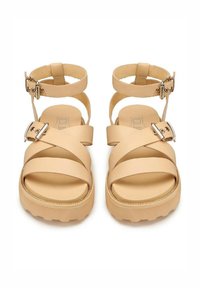 Sandali platform beige con design a fascette incrociate, chiusura a fibbia alla caviglia, materiale sintetico liscio e suola in gomma testurizzata.