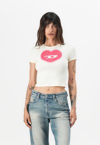 White ribbed crop top featuring a pink heart graphic with a white symbol in the center. Pairing with distressed blue denim jeans.
