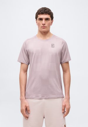 Man standing facing forward wearing a light mauve short-sleeve patterned athletic shirt and matching shorts on a white background.