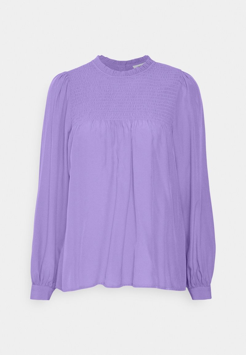Blouse longue à manches longues en lavande avec empiècement smocké, col à volants, tissu froncé sous la poitrine et poignets boutonnés sur un fond uni.