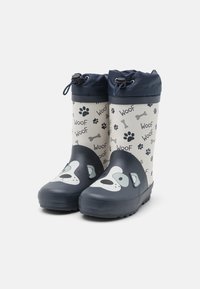 Bottes de pluie imperméables pour enfants, avec une base bleu marine, un motif de visage de chien, une partie supérieure beige avec des empreintes de patte, et une fermeture supérieure ajustable.