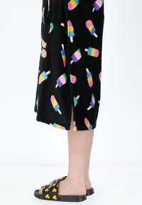 Robe nera con motivo di ghiaccioli colorati in tessuto morbido; indossata sopra sandali neri con grafica di anatra gialla. Gamba visibile all'orlo.