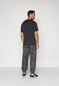 Μαύρο κοντομάνικο t-shirt συνδυασμένο με γκρι jogger με σχέδιο. Οι jogger έχουν ελαστικά μανσέτα και πλευρικές ρίγες, ολοκληρώνοντας μια αθλητική εμφάνιση.