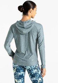 Grauer sportlicher Hoodie aus texturiertem Stoff mit Kapuze, kombiniert mit blauen Leggings mit Mustern, die abstrakte Designs und eine figurbetonte Schnittführung aufweisen.