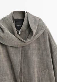 Giacca con zip in tessuto grigio a trama, collo ampio a scialle e tasca frontale, con etichetta Massimo Dutti.