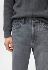 Jeans de mezclilla gris con un ajuste relajado, diseño de cinco bolsillos y una textura sutilmente deslavada. Combinados con un suéter de punto oscuro.