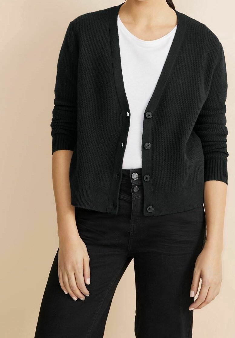 Black knitted cardigan with a V-neck, front buttons, ribbed cuffs, and a textured fabric, worn over a white t-shirt and black jeans.