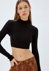Czarny prążkowany crop top z długimi rękawami i wysokim dekoltem, w połączeniu z brązowymi spodniami w wężowy wzór z zapięciem na guzik.