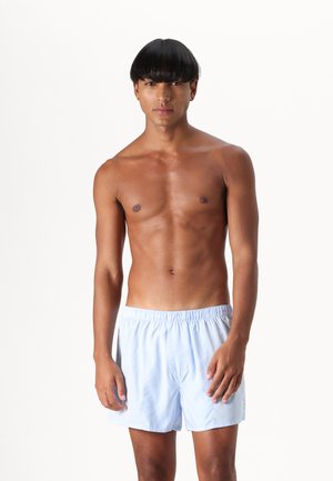 Shorts de bain bleu clair avec une taille élastique, fabriqués en tissu lisse ; coupe longueur genou, présentant un design minimal sans motifs visibles.