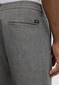 Gray tailored trousers with a textured fabric, featuring a back pocket and a small brand label stitched on the waistband.